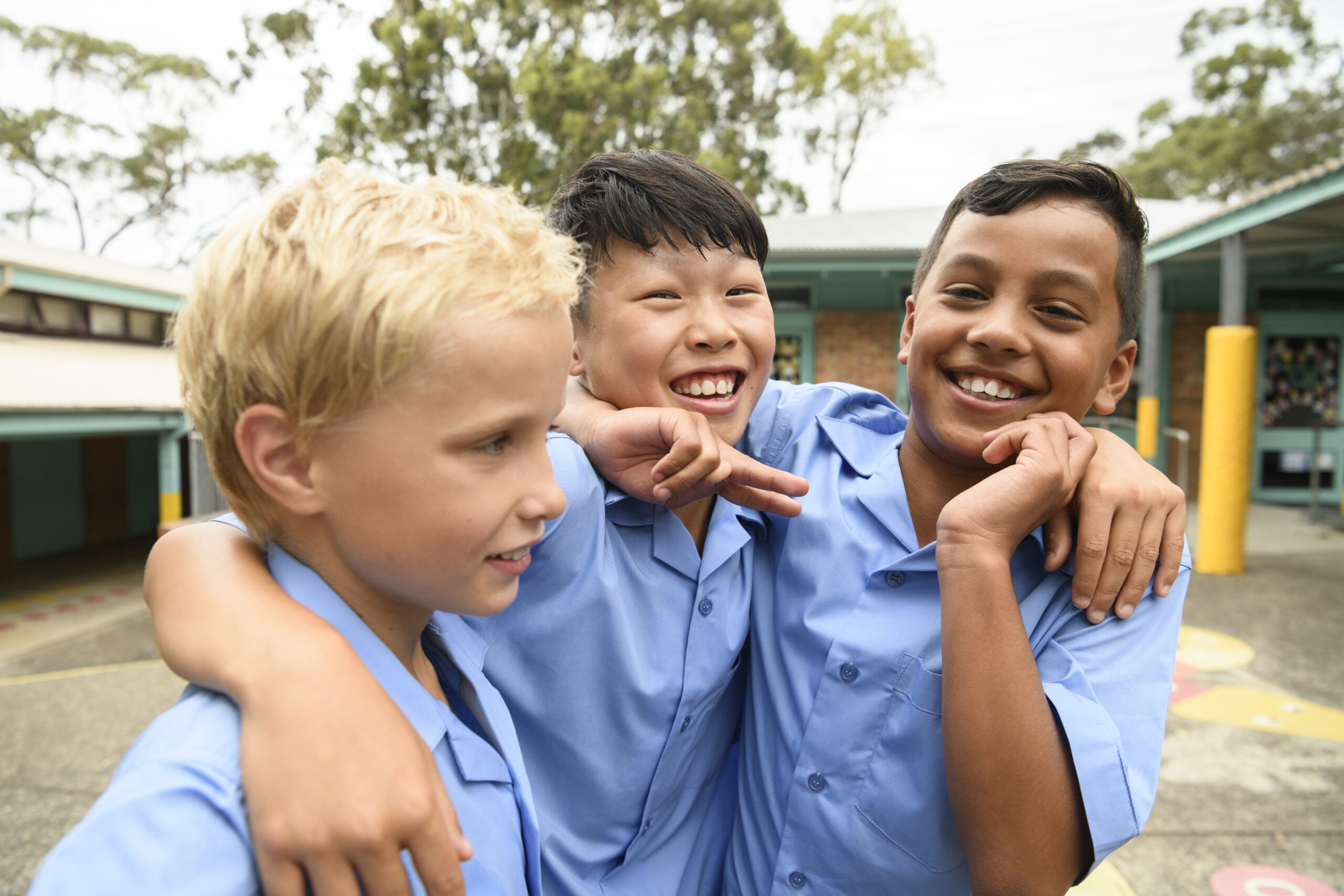 Candid portrait of three boys in school playground with arms around each other